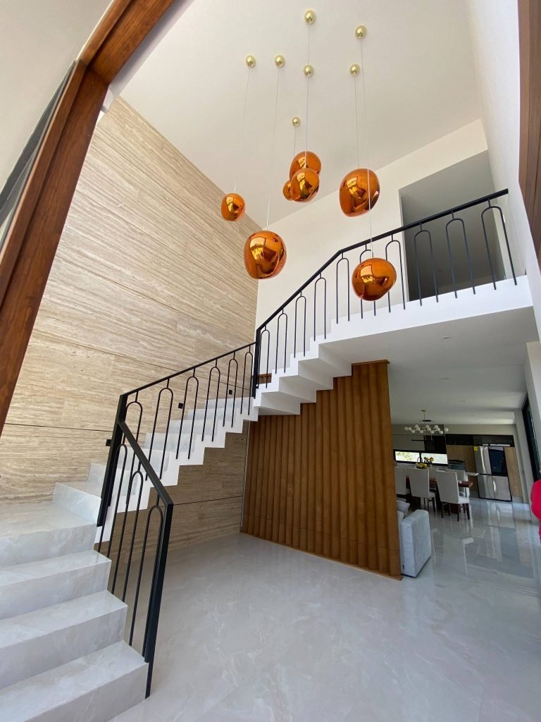 Diseño de vestíbulo con escaleras y lámparas colgantes doradas que realzan la elegancia del espacio.