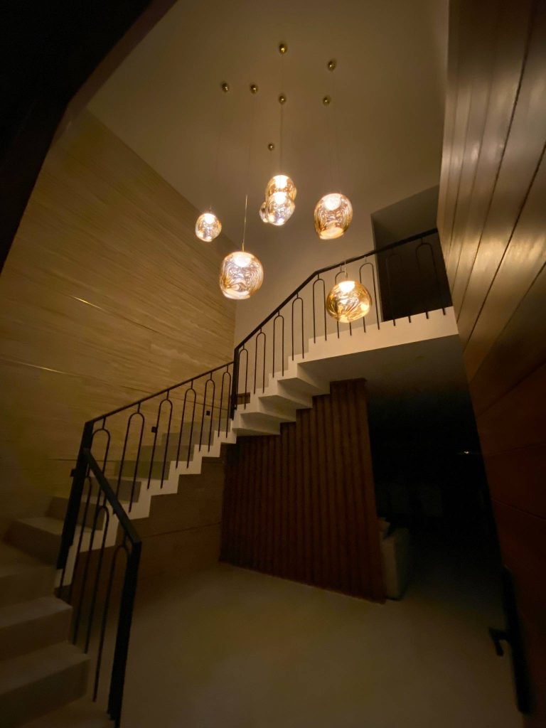 Escalera y entrada iluminada con lámparas doradas, creando un ambiente cálido y sofisticado.