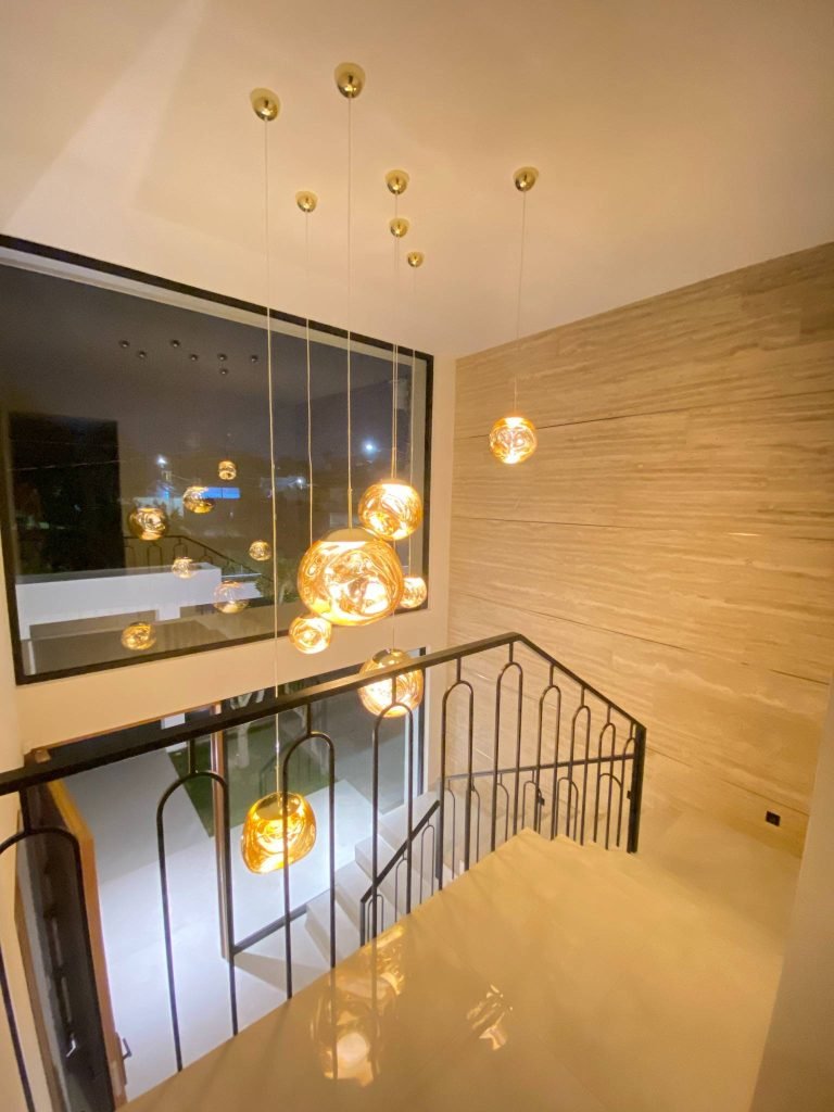 Detalle arquitectónico del vestíbulo con iluminación colgante dorada y acabados contemporáneos.