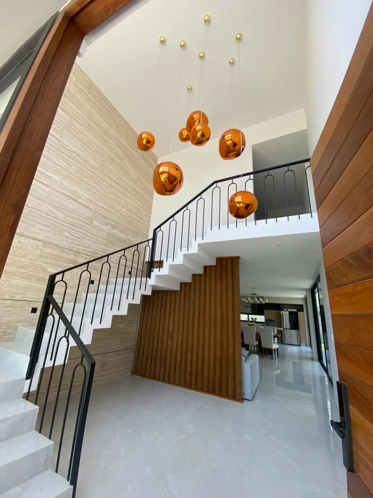 Diseño de interiorismo residencial en Querétaro. Vestíbulo moderno con iluminación colgante y acabados en mármol y madera.