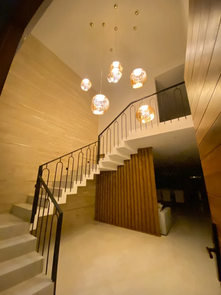 Interiorismo residencial en Querétaro. Vestíbulo elegante con lámparas colgantes doradas y acabados contemporáneos.